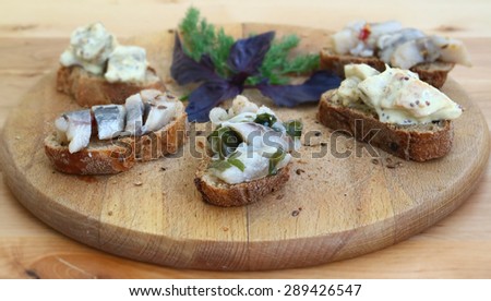 Sandwiches of rye bread and herring. Pieces of fish are herring on bread. Sandwiches with byboy on a wooden boards background. Traditional food for the reception. Fish dishes. Scandinavian cuisine.