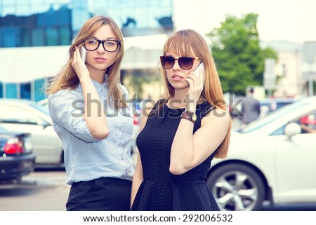 Two business women talking on mobile phone. Two young modern beautiful women. Two stylish women talking on a mobile phone. Woman on the background of the city. Happy girls student. Phone conversation