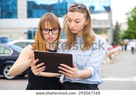 Women using tablet. Two business women using a tablet computer. Two young modern beautiful women on the background of the city street. Girls student. Two attractive women sharing ideas on a touch pad.