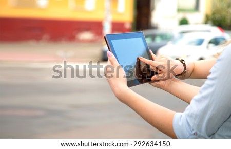 Close up hand presses on screen digital tablet. Two women hands with tablet computer and phone on the city. Closeup of women hands holding electronic tablet on a background of city streets and cars.