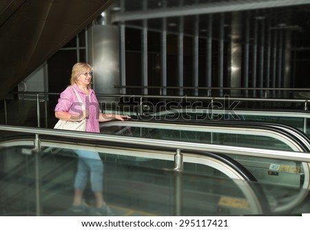 Adult woman walking on the escalator. Woman holding a big bag, carry-on baggage. Woman Trips, she goes on an escalator in the station building, an airport, a subway station. Lifted by escalators.