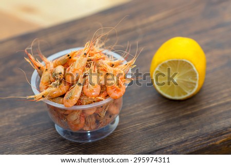 Delicious fresh cooked shrimp prepared to eat. Cooked shrimps with lemon on wooden table. Snack to beer and wine. Shrimp from the Black Sea. Serve cooked shrimp and lemon on a bar table.