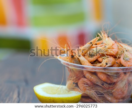 Serve cooked shrimp and lemon on a bar table. Delicious fresh cooked shrimp prepared to eat. Cooked shrimps with lemon on wooden table. Snack to beer and wine. Shrimp from the Black Sea.