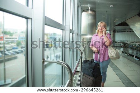 Adult woman talking on a cell phone. She travels. Make a phone call while roaming. Woman is traveling. Talk on the phone at the airport or station of transit. Arrange a meeting in another city. Trip.