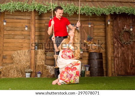 Pregnancy woman and man happiness. Beautiful young man and woman is expecting a baby, she is pregnant. Pregnant woman in bright color dress sitting on a swing against the backdrop of a country house.