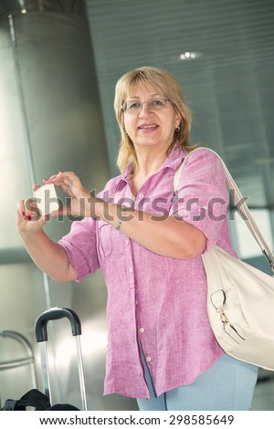 Adult woman smiling and talking on a smart phone. Happy woman her cell phone. Traveler with mobile phone in airport. Tourist woman with travel bag. Take photos on your mobile phone.