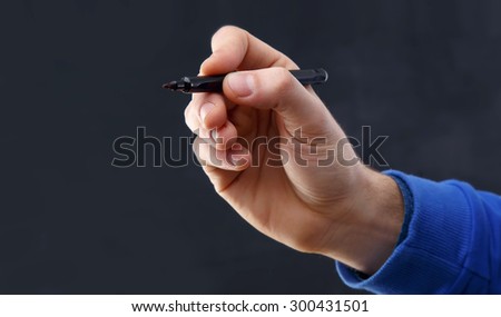 Close up of a man\'s hand with a marker on a gray background. Man\'s hand with a pen in the air makes the sign close up, concept
