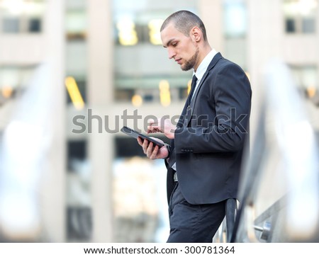 Manager. Businessman working for digital tablet on the background office center building. Working out of the office. Young arab business man writing something in his note pad and at not looking camera