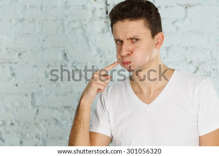 Young man in pain is having a toothache. Man having toothache. A man has a toothache. Young handsome sad man in white shirt points to swollen cheek, he had a toothache.