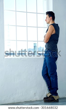 Man looking out the window. Fashionable man standing near a window looking out into the distance. Creative portrait. Concept - sad, sadness, grief, loneliness, waiting, watch, wait - emotion man.