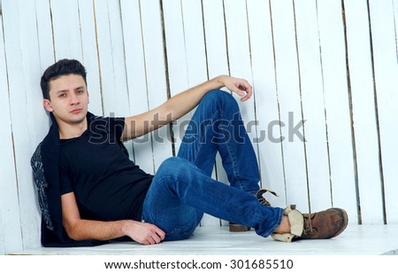 Man model posing on a light background of blue wood. Portrait of young beautiful fashionable man against wooden wall. Jeans fashion man with short dark hair. Wearing blue jeans, jacket. Modern man.