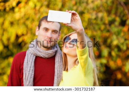 Close up - couple in the autumn park taking selfie with mobile phone. Smiling couple taking selfie with smart phone in the city park. Couple in the autumn garden. Couple taking selfie photo.