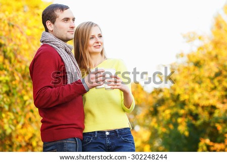 Happy couple with coffee cups in autumn park. Love story concept. Man and woman drinking tea or coffee on the background of autumn park. They are holding paper cups. Picnic. Drink warm in cool weather
