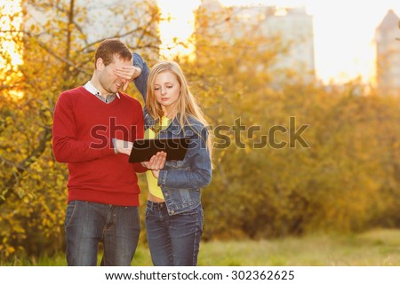 Couple in autumn garden. Man and woman together ordinary people. They are holding electronic tablet. Watch E-book. Emotional couple in love. Young couple using electronic tablet in autumn park.