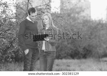 Man and a woman together. Black and white image. Young people are holding electronic tablet. Watch e-book. Emotion woman. Couple love. Girl surprised. Woman is shows what is on the electronic ps, pad.