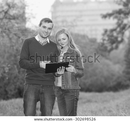 Couple in city garden. Man and woman together ordinary people. They are holding electronic tablet. Watch E-book. Emotional couple in love. Young couple using electronic tablet in autumn park. print