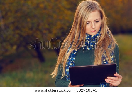 Young woman using tablet computer on autumn city park and street. Woman working on digital tablet outdoors in the park. Modern student woman using tablet pc outside on a autumn garden. Woman using pc