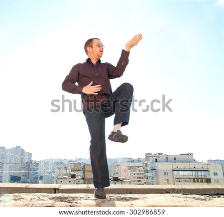 Serious man studied oriental martial arts on the roof of a skyscraper during the working break. Business man doing gymnastics exercises karate on the roof of a skyscraper on a background of blue sky.