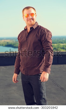 Portrait of confident mature man smiling. Outdoor portrait of handsome man posing at blue sky, in nice sunny day, beautiful view on blue sky, wearing casual classic brown shirt and sunglasses. Life.