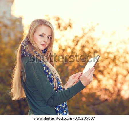 Beautiful happy woman using digital tablet outdoor. Young woman using tablet computer on autumn city park. Woman working on his tablet outdoors in the park. Modern woman using tablet pc outside. Life