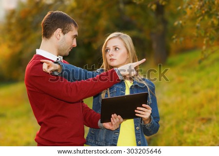 Man and woman holding electronic tablet in hands, argue where to go. Point the finger in different directions. Young students. September, October, golden autumn. Traveler, tourist, navigator, lose.