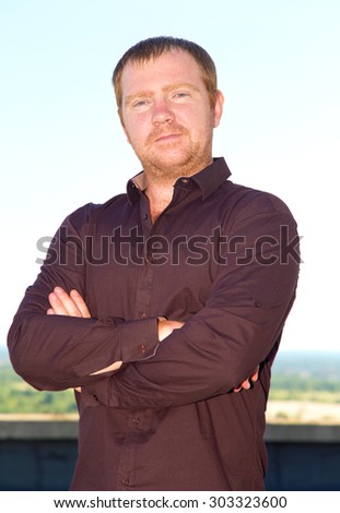 Portrait of the red hair man on the blue sky background. Portrait of a serious confident man crossed his arms. Modern business man.