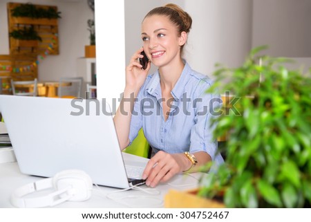 Businesswoman at workplace. Portrait beautiful woman on the background of modern business office. Young business woman working in office. Woman student talking on cell phone. Green office. Life style.