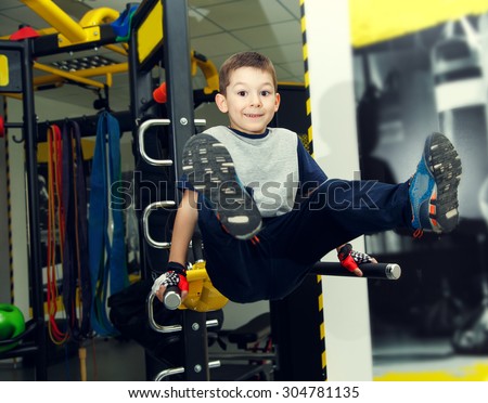 Sports boy in the gym. The child has been on the uneven bars. Surrounded by sports equipment. Sporty boy. Happy boy holding different sports equipment while standing club.