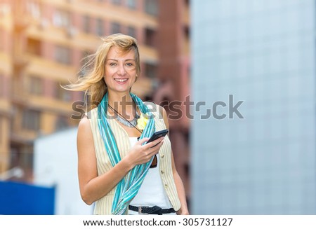 Happy woman. Woman in the street in sunshine light. City lifestyle stylish hipster girl using a phone text on smart phone app in a street. Woman in white shirt reads or text message to mobile phone.