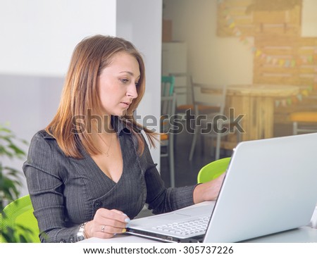 Business woman sitting in the office. Working using a laptop ps. Office people sitting at desk and working. Woman using laptop computer. Remain after working. Come earlier. Working from dusk till dawn