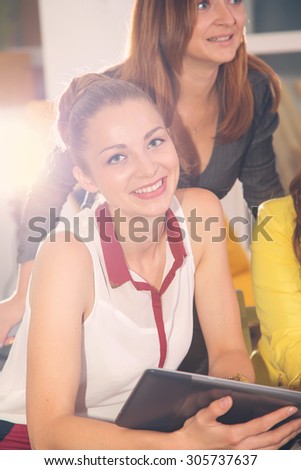 Beautiful modern student woman holding tablet computer with colleague on background. Young woman using tablet in business training. Cheerful group of students or colleagues in the room school office.