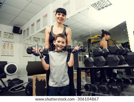 Woman mother with boy and dumbbell in hands in health club. Joint exercise sports with the child. Family mother and son holding different sports dumbbells while standing close to each other in gym.