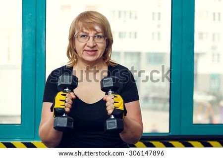 Woman holds up lifting dumbbells. Client fitness center. Woman - fitness gym. Senior exercising at gym. Old woman exercising with weights at gym. Adult woman holding dumbbell lifting up. Sport woman.