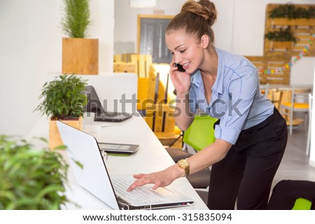 Young female office worker talking on a cell phone. Business woman calling on the phone in working environment. Woman. Smart phone. Customer service. Beautiful young woman at working place in office.