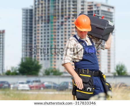 Man builder. Handyman with a tool belt. Male builder. Construction worker holding a tool box. Construction worker on a construction site. Renovation, service.