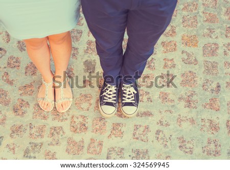 Legs close up. Fashion summer of hipster couple. Close up of feet. Man and woman posing on the city street. Blue dress woman. Man\'s sneakers and denim.
