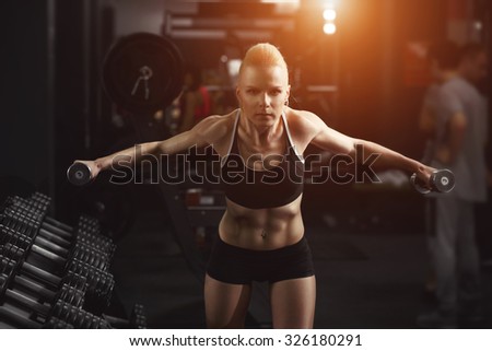 Fitness Woman doing exercises to warm up your muscles. Sporty woman in gym. Female holding barbells. Young woman, sport, workout - advertising concept. Blond woman in sport wear. Perfect fitness body.
