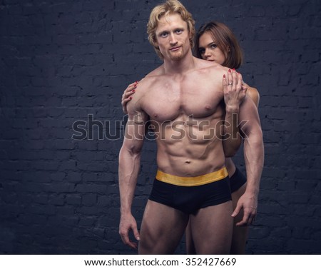 Sexy sport couple man and woman on a dark brick wall. Athletic. Couple in underwear. Strong man and a woman posing on a black background. Place for posts, copy space. Sexual couple.