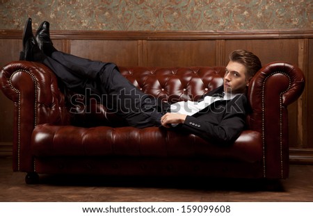 a man in a suit lying on the couch and looking at the camera