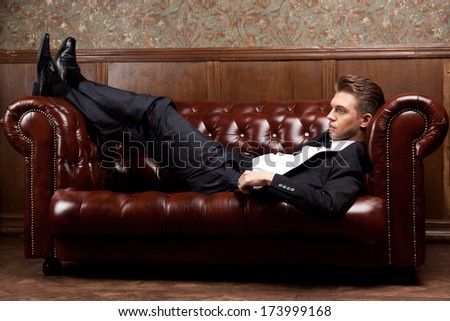 Attractive Young Man In A Suit Sitting On A Retro Couch