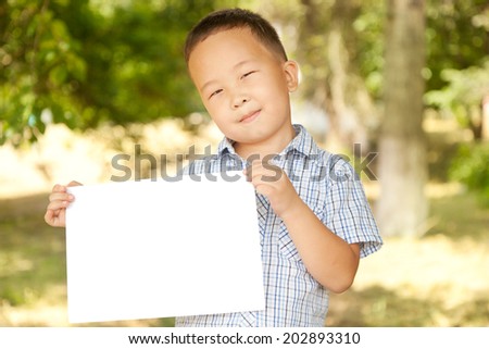 Asian boy  6 years old with a sheet of paper in the park, smiling