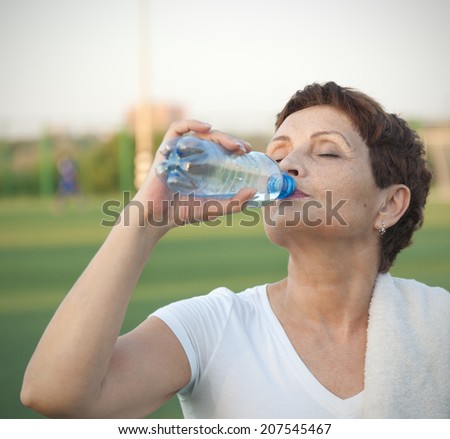 attractive woman 50 years old, drinking water after fitness, outdoors