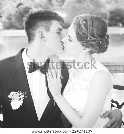attractive bride and groom kissing, sitting on a bench, black and white image