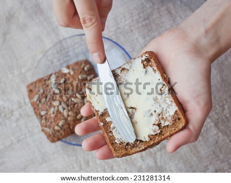 woman hand  rubs butter on piece of rye bread