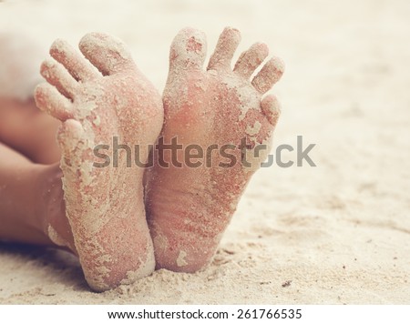 funny woman\'s feet on the white sand near the sea
