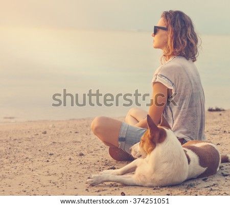 young woman with her dog on the beach watching the sunset