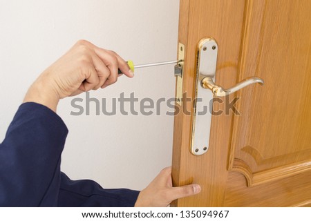 Carpenter fixing a lock in the door  with a screwdriver on close up