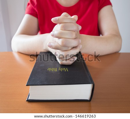 women hands folded in prayer over a holy bible closed