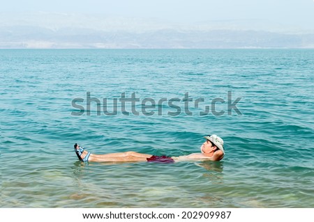 Man floating in a glassy water of dead sea with outstretched arms