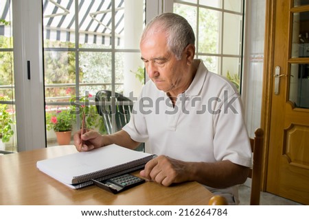 Unhappy old man calculating the monthly expenses at home